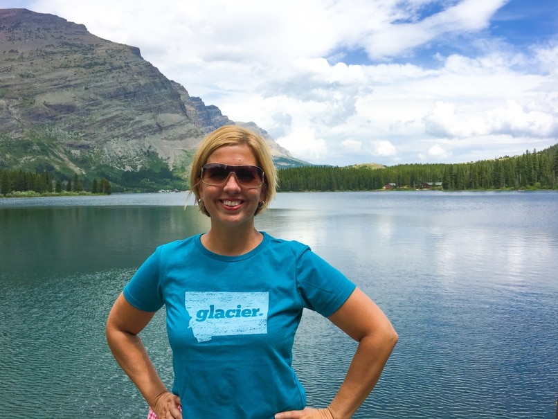 woman wearing glacier national park t-shirt standing in front of lake
