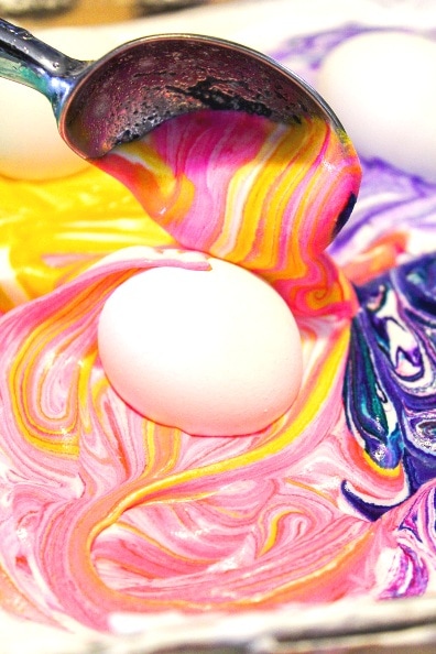 white egg with colored whipped cream in a spoon covering it