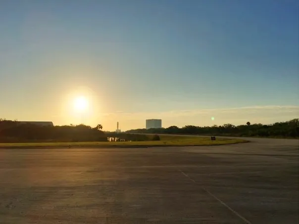 a mobile rocket launch tower and a large building on the horizon as the sun rises