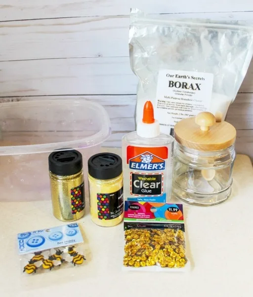 glitter glue bottle sequins bee buttons and bag of borax on a table for slime recipe