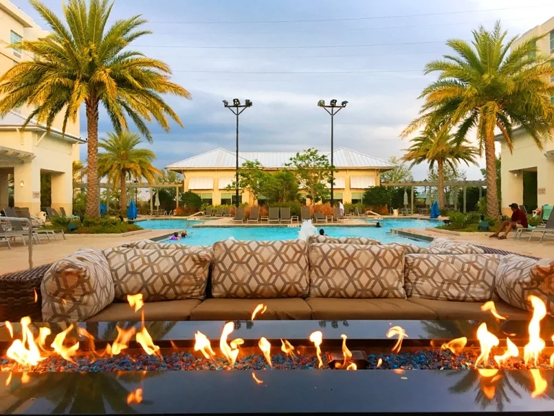 firepit with flames by pool surrounded by palm trees