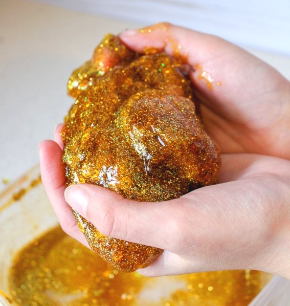 child's hands holding honey colored slime with gold glitter and sequins 