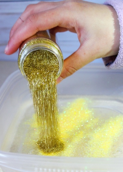 gold glitter being poured into a plastic container of clear glue