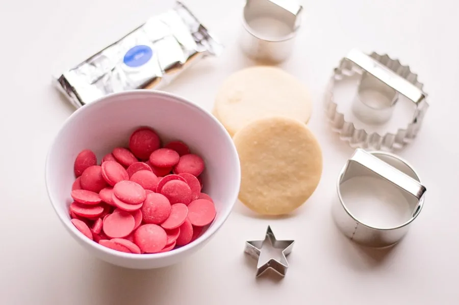 white bowl of red candy melts sugar cookie star cookie cutter circle cookie cutters on white table