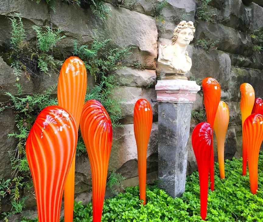 red and orange glass sculptures against stone wall with bust