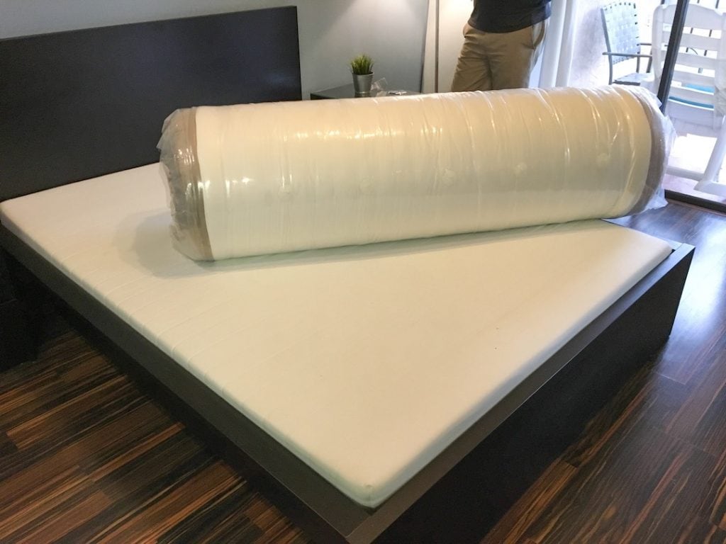 Dreamcloud mattress rolled up in plastic laying on a bed