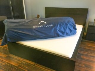 Dreamcloud mattress rolled up in a blue duffel bag lying onto of bed frame
