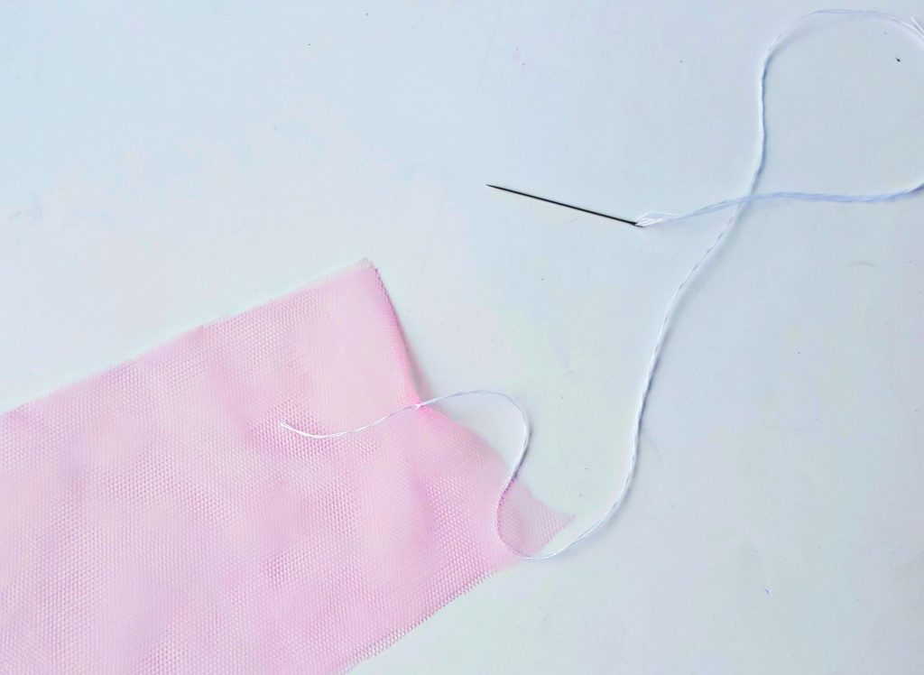 sewing together two pink mesh tulle strips with needle and white thread