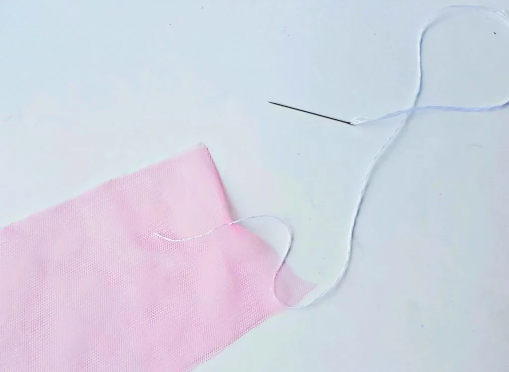 sewing together two pink mesh tulle strips with needle and white thread