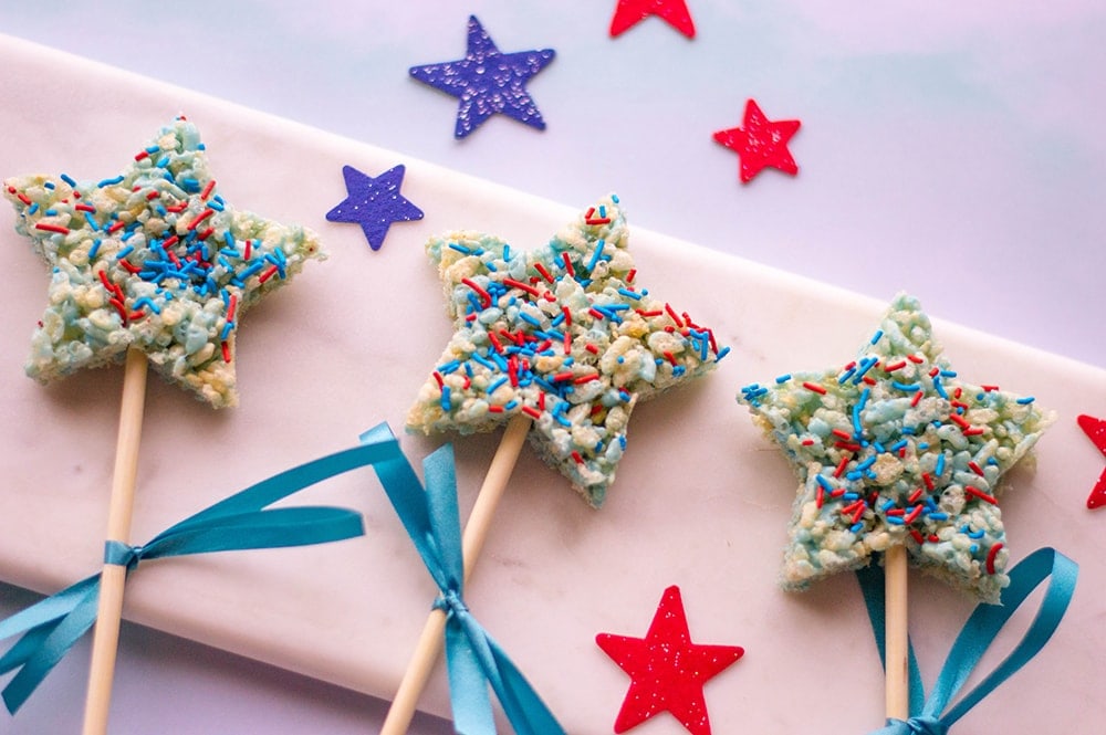 star shaped Rice Krispies treats with blue and red sprinkles on a pink background