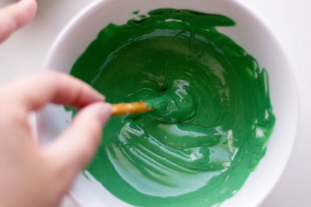 dipping a pretzel stick into green frosting to make Star Wars light sabers