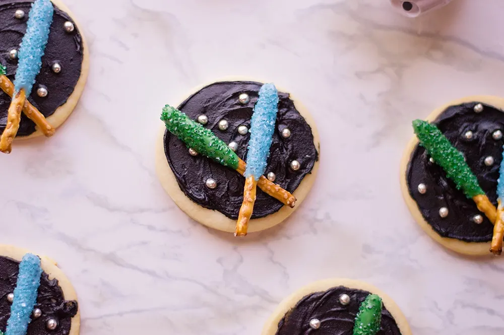 sugar cookies with black frosting and Star Wars light sabers on top made from pretzel sticks