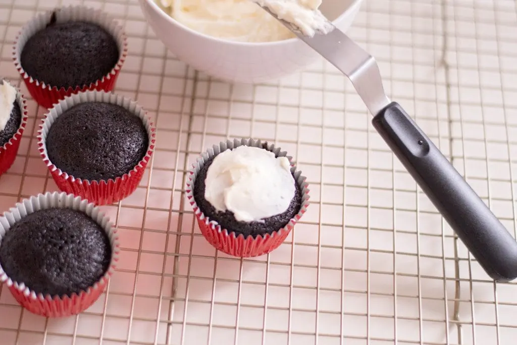 chocolate cupcake with red wrapper topped with white frosting on a baking rack