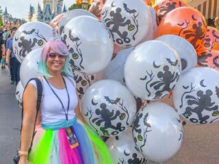 rainbow tulle skirt unicorn costume holding halloween balloons in front of castle at Disney world