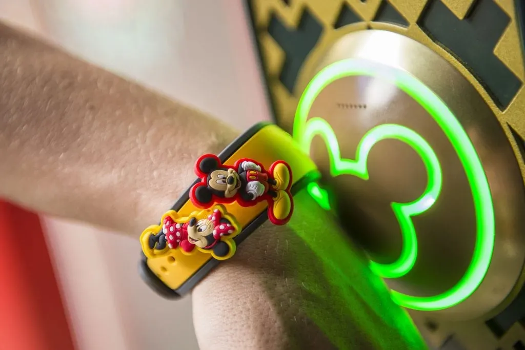 Person wearing a yellow bracelet with Mickey and Minnie Mouse buttons attached