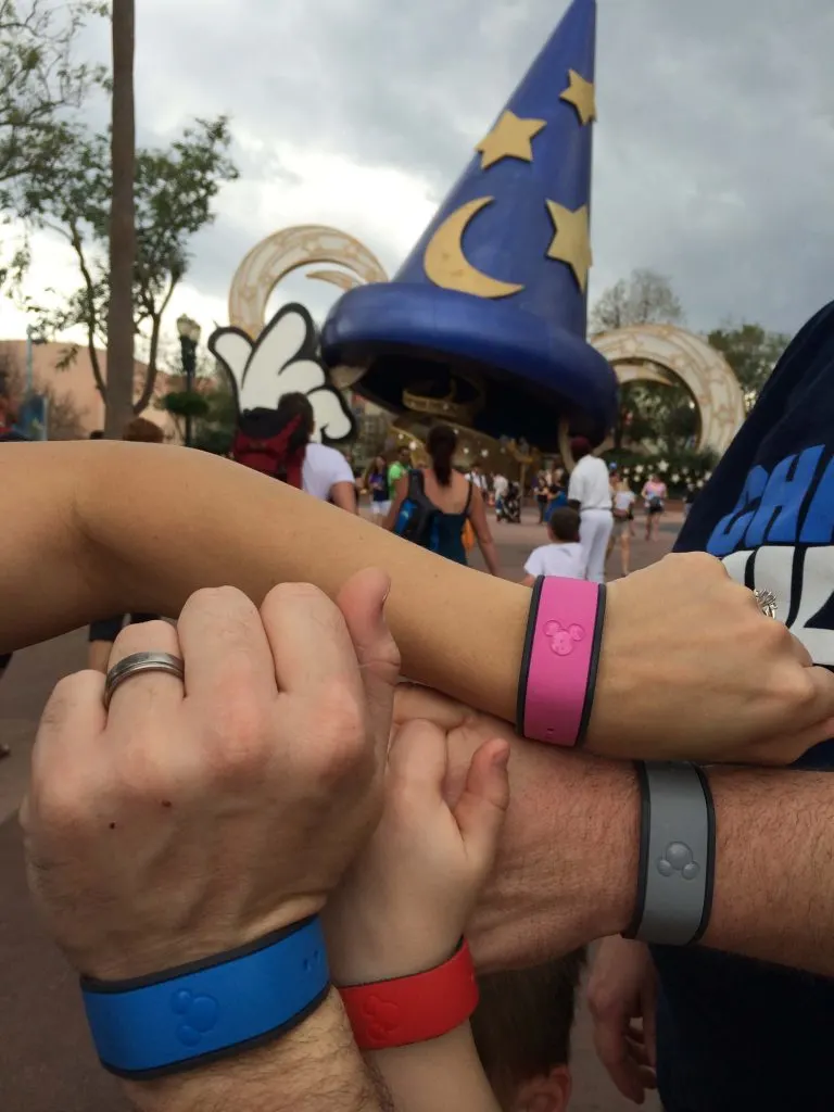 family wearing Disney MagicBands in many colors in front of Sorcer Mickey Hat 