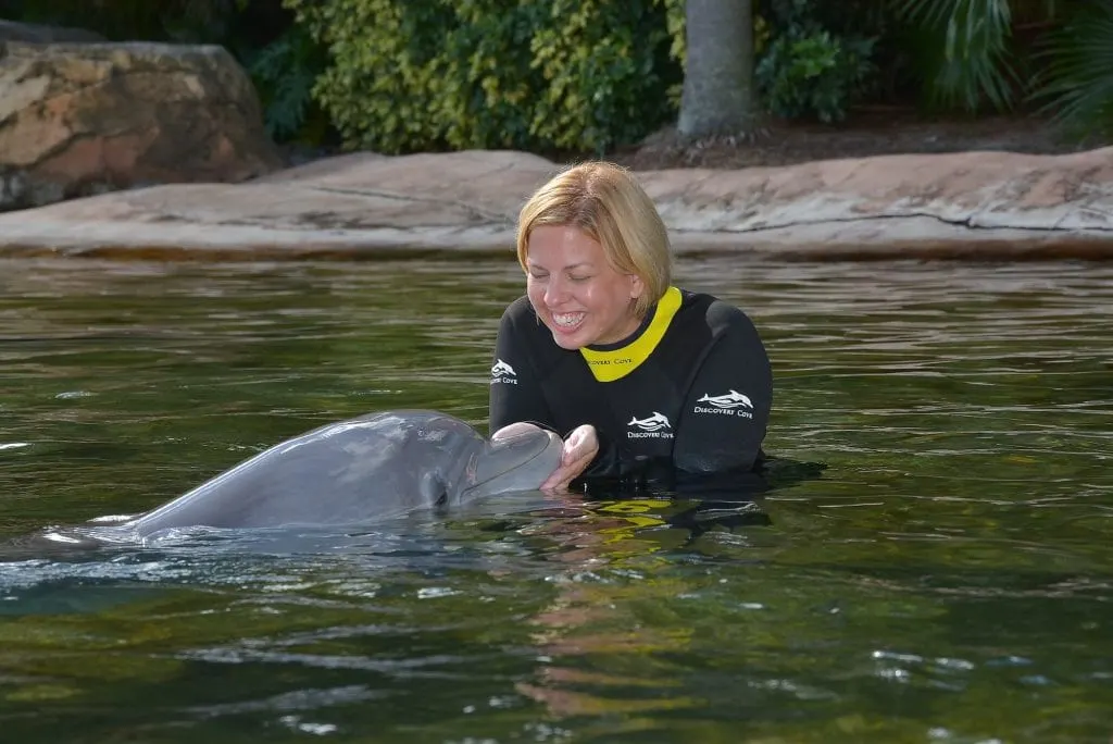 woman holding dolphin in shallow water and smiling Discovery Cove Orlando Florida