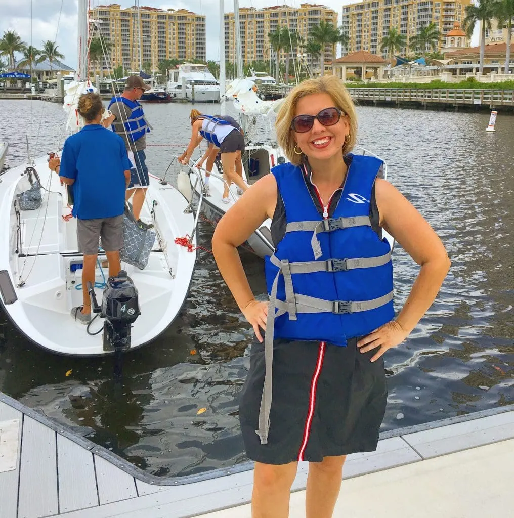 woman in life jacket standing on dock in marina in front of offshore sailing school boat Cape Coral FL