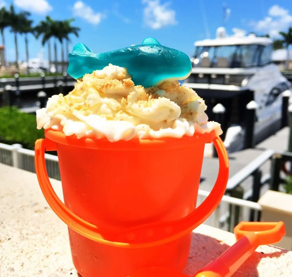 orange plastic sand pail filled with ice cream and topped with whipped cream with blue candy shark on top against marina background at Westin cape coral fl