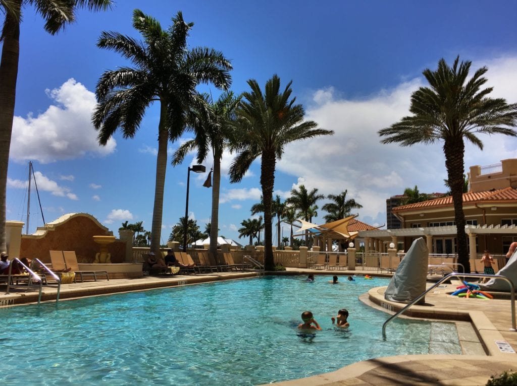 blue green water in pool under tall palm trees with kids playing in water