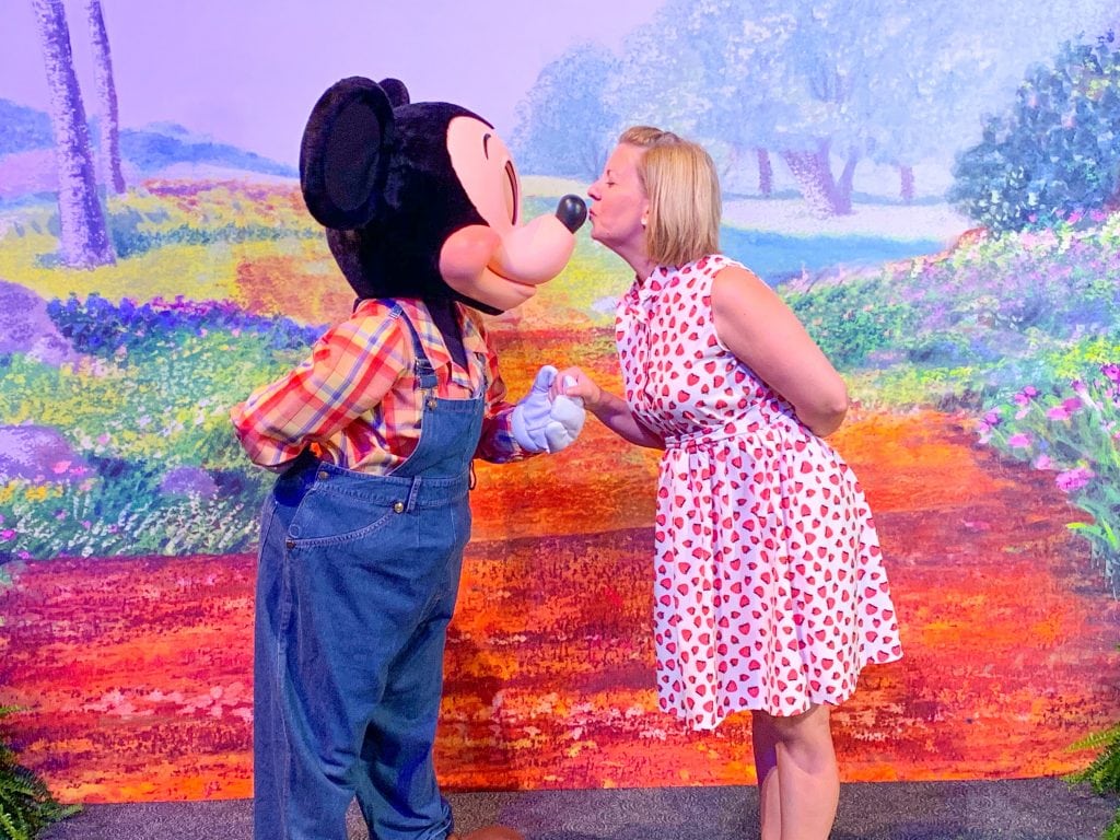 woman kissing Mickey Mouse on the nose with a garden scene in the background
