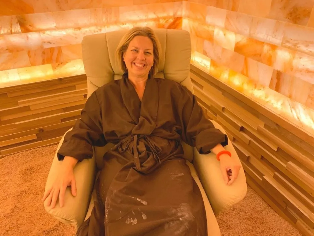 woman in brown robe sitting in lounge chair in Himalayan pink salt therapy room 