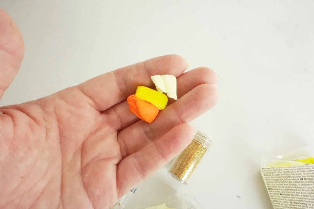 orange yellow and white pieces of clay in woman's hand against white background