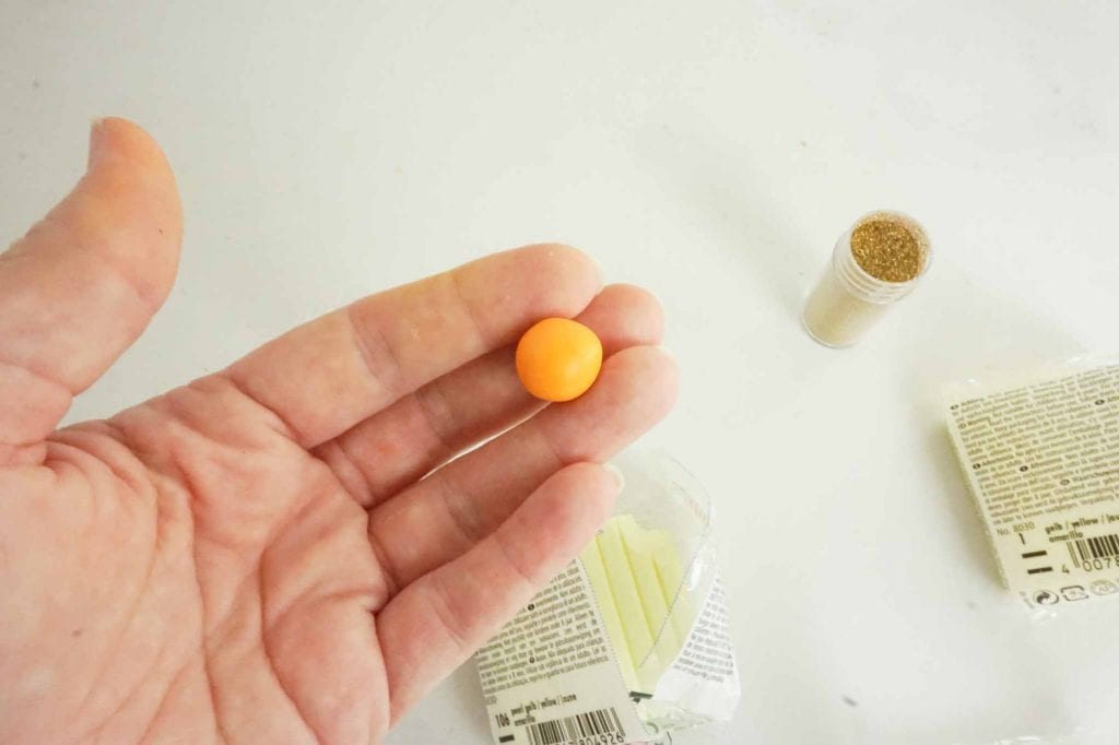 rolled orange clay ball in woman's hand against white background