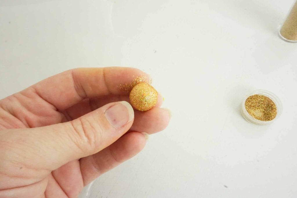 golden ball of clay covered in glitter in woman's hand against white background