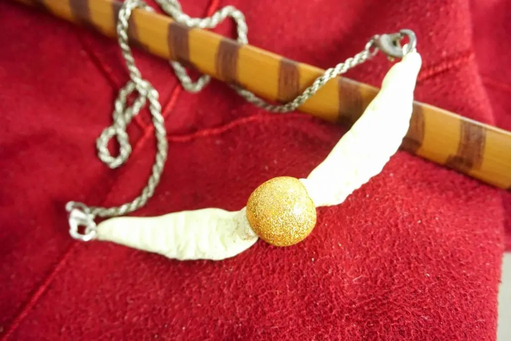 golden snitch ball with wings necklace on red background with wand