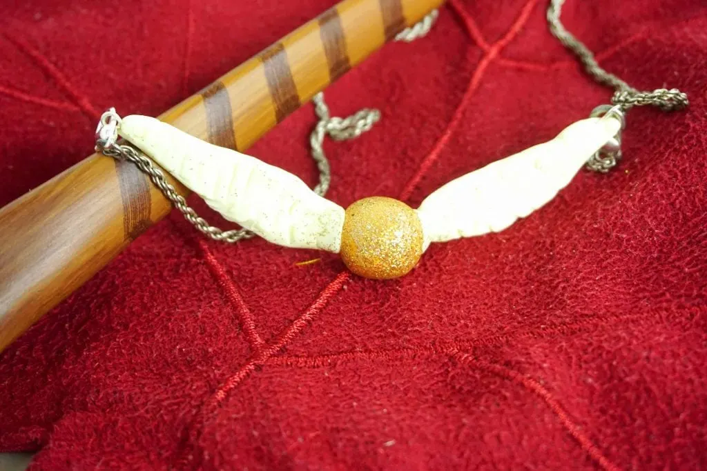 Golden Snitch Ball with Wings Necklace on red background with Harry Potter wand