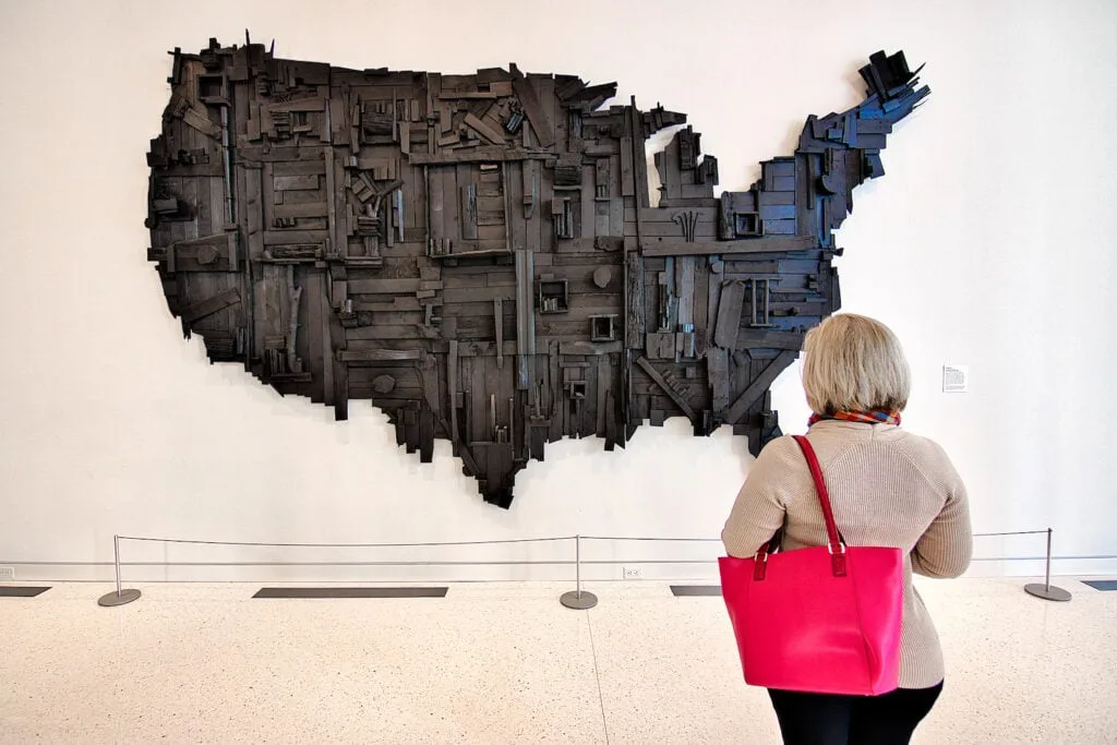 woman holding pink purse looking at wooden United States artwork