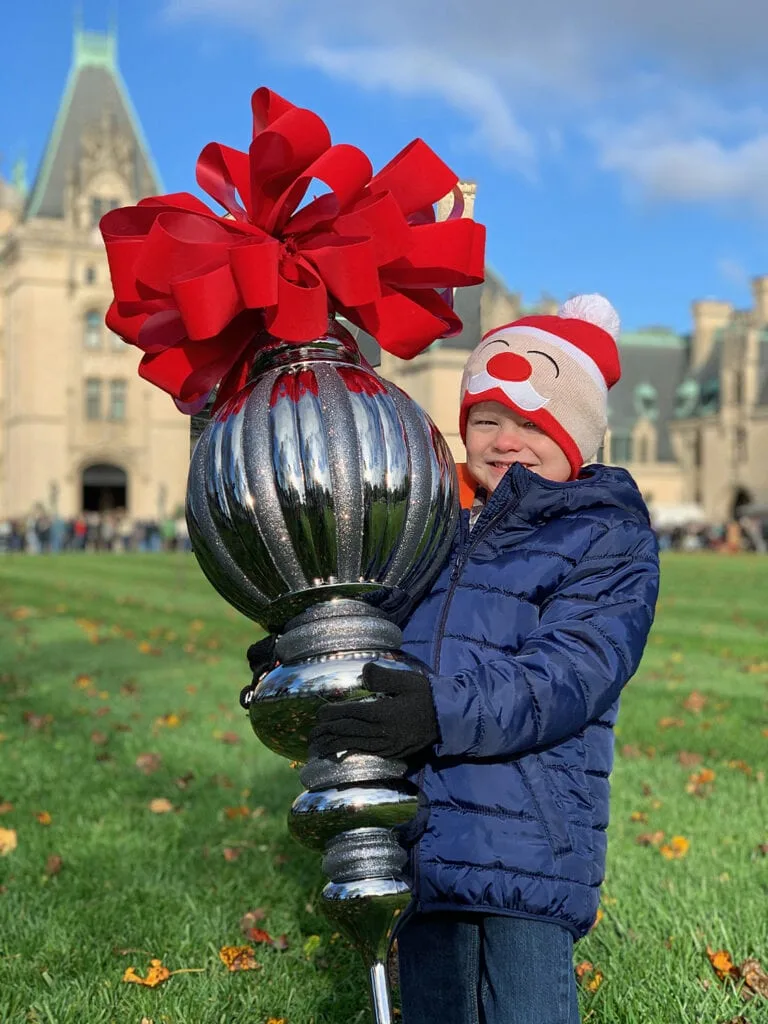 boy holding large Biltmore Christmas ornament in front of house