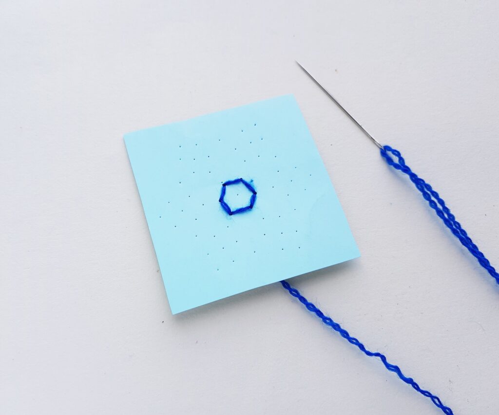 stitching a snowflake string art pattern with blue yarn and needle