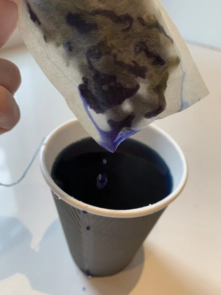tea bag with blue tea dripping into a cup