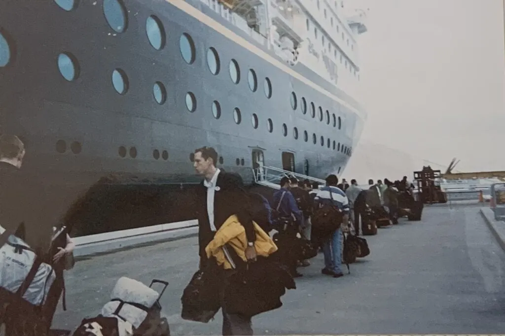 cruise line workers holding luggage getting on ship