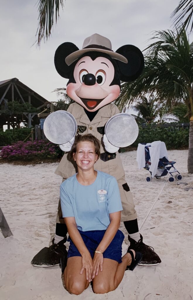 woman sitting in sand with Mickey Mouse behind her