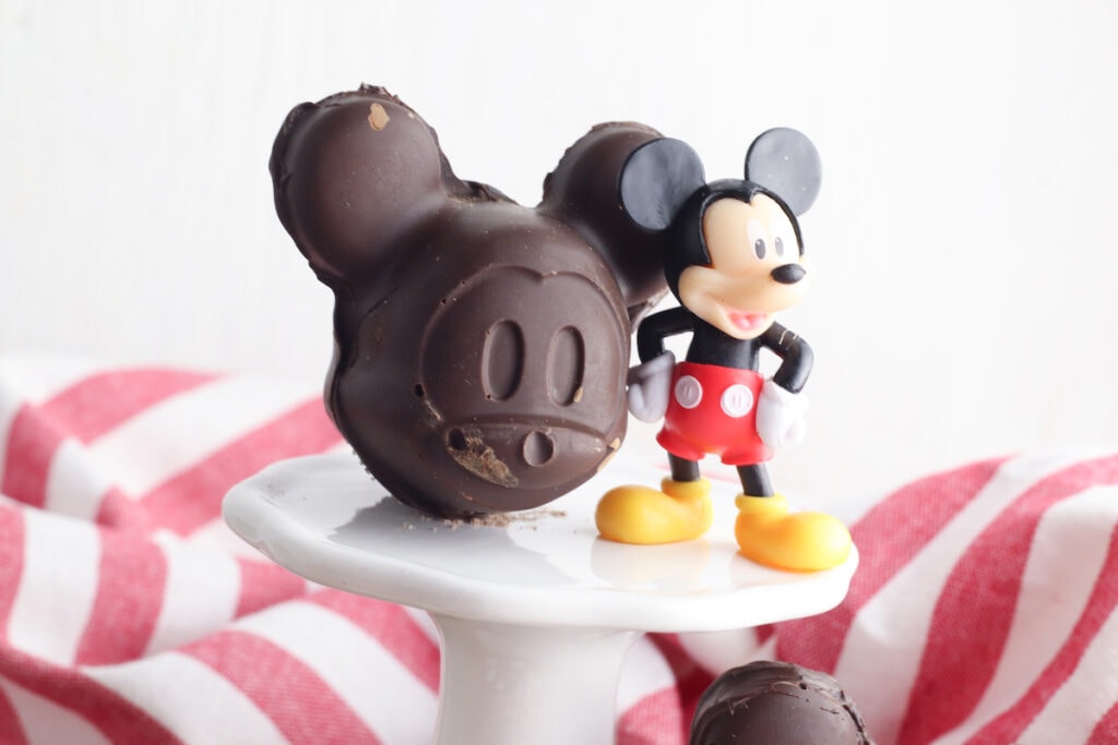 mickey shaped chocolate mold on white pedestal next to plastic Mickey Mouse figurine
