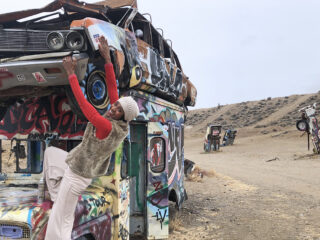 woman climbing on stack of graffiti covered old cars in Nevada desert
