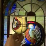 holding a glass of hard cider in front of a colorful stained glass window