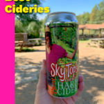 can of hard cider held in front of apple orchard