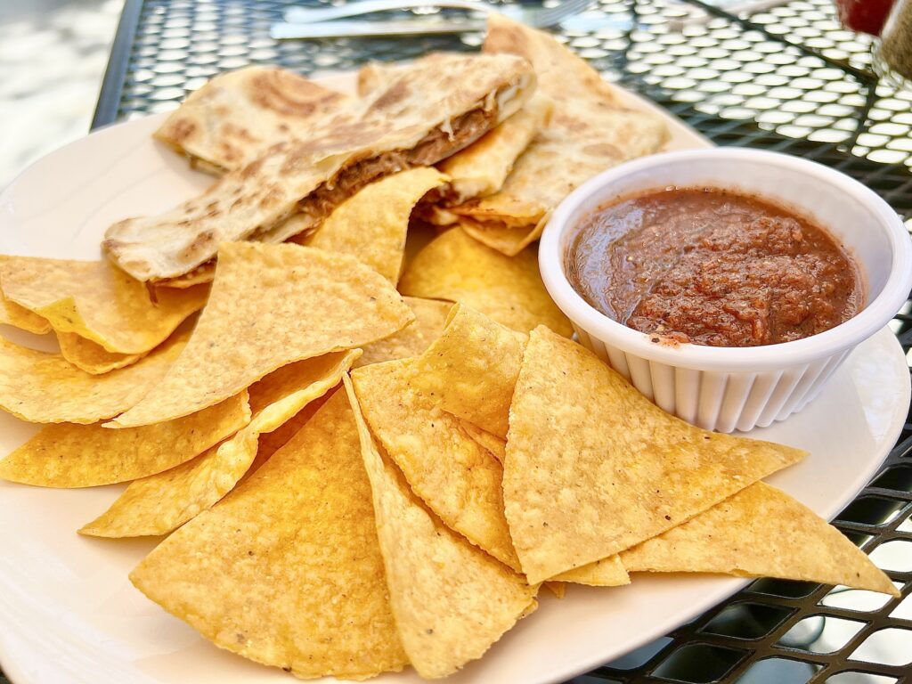 chips and bowl of salsa next to quesadilla on white plate