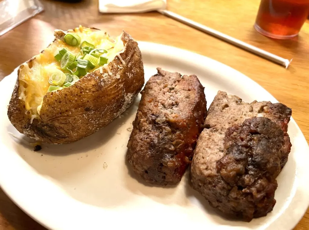 white plate with two slices of meatloaf and a loaded baked potato