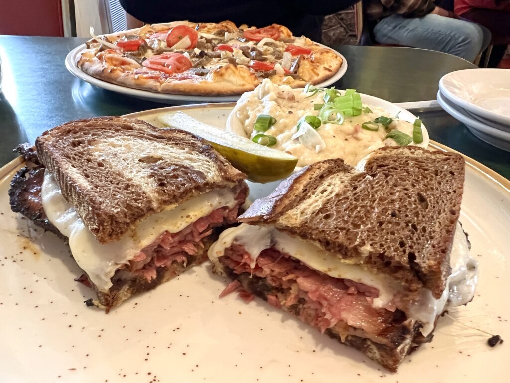 pastrami sandwich on rye bread with Neapolitan pizza in background