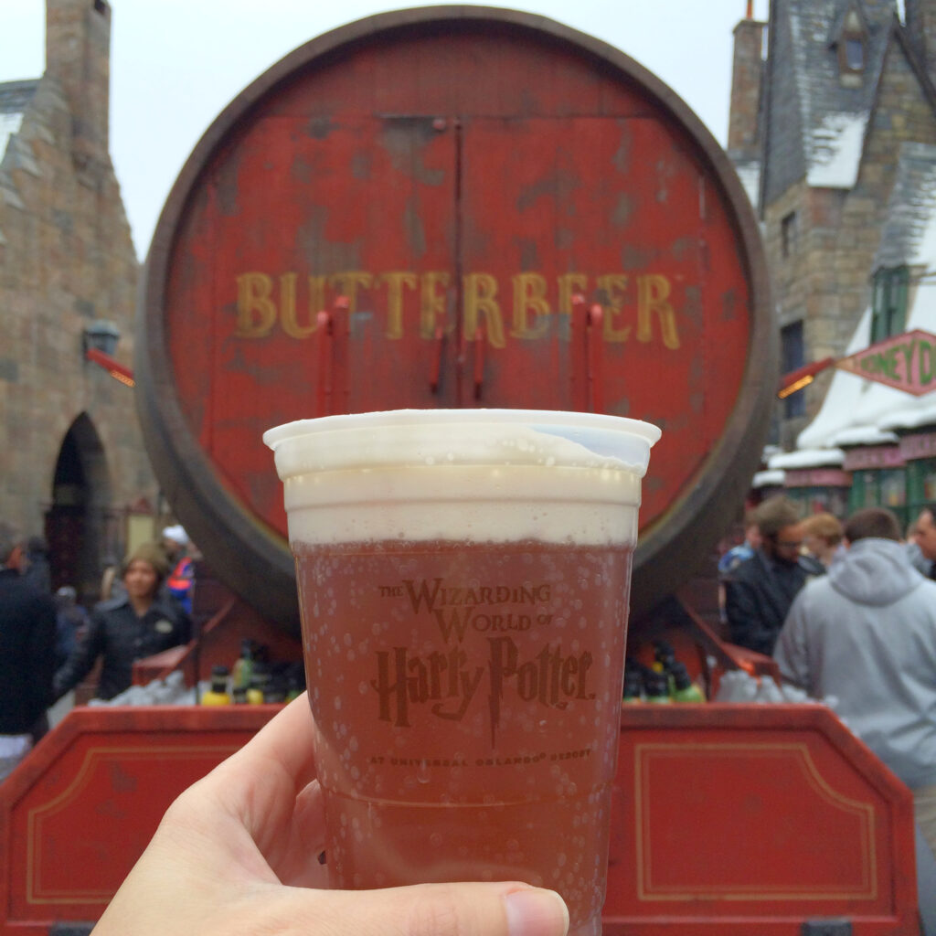 holding a cup of butterbeer in front of a barrel in Harry Potter land