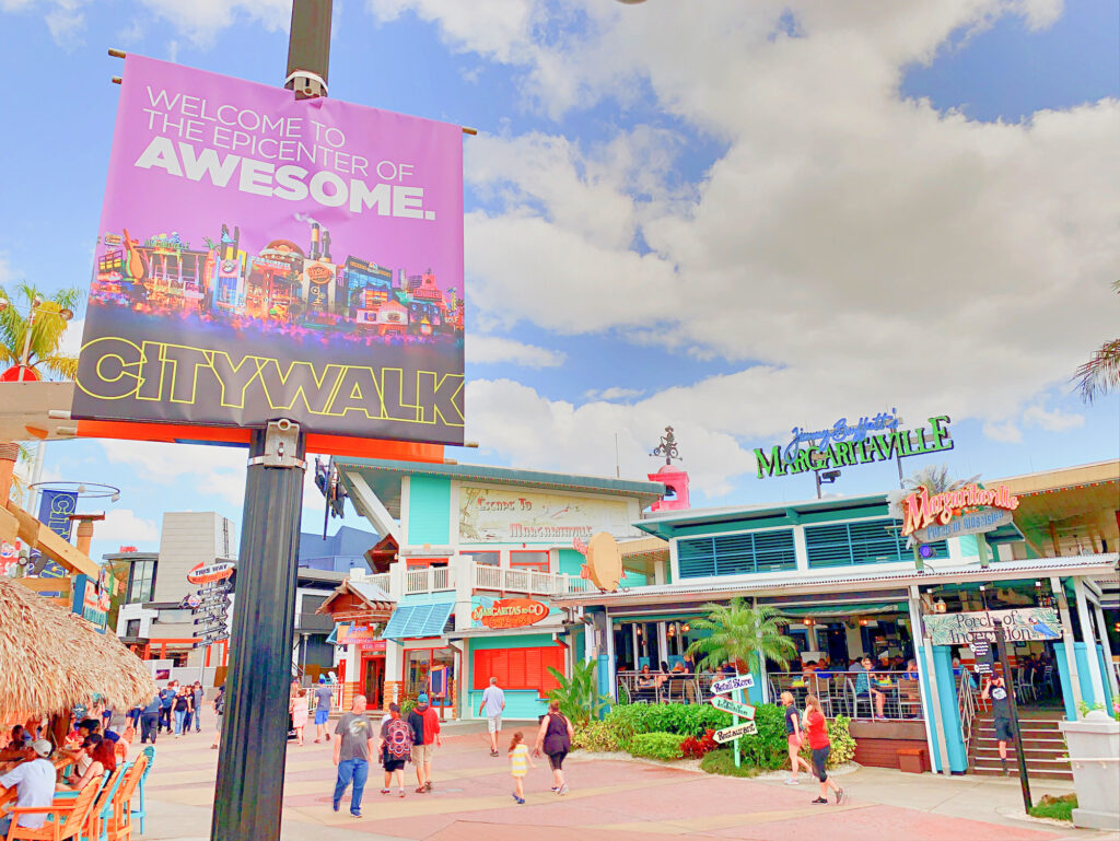 Universal Citywalk pathway with people walking by restaurants and large welcome sign in foreground