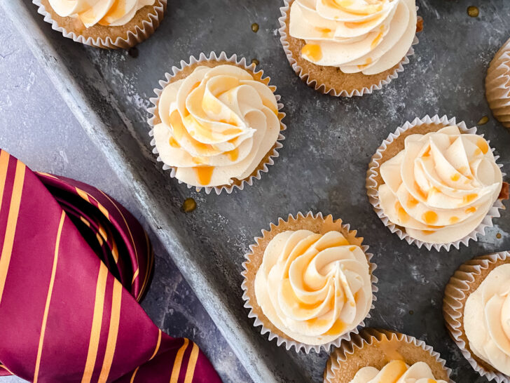 butterbeer cupcakes on baking sheet next to maroon and yellow striped tie and Harry Potter glasses