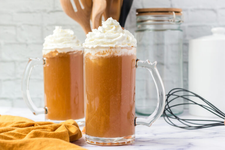 two glass mugs of butter beer beverage topped with whipped cream