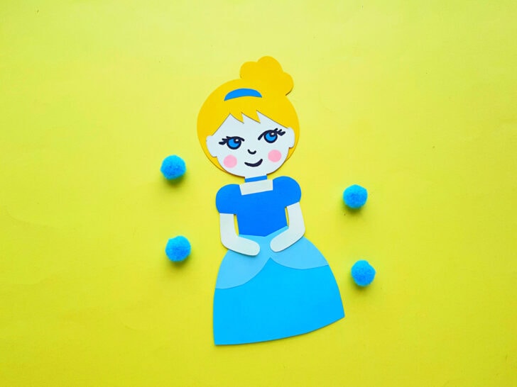 Cinderella paper doll on a yellow back ground with four blue pom poms