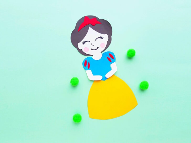 pretty Disney princess Snow White paper doll on a green background with four green pom poms nearby